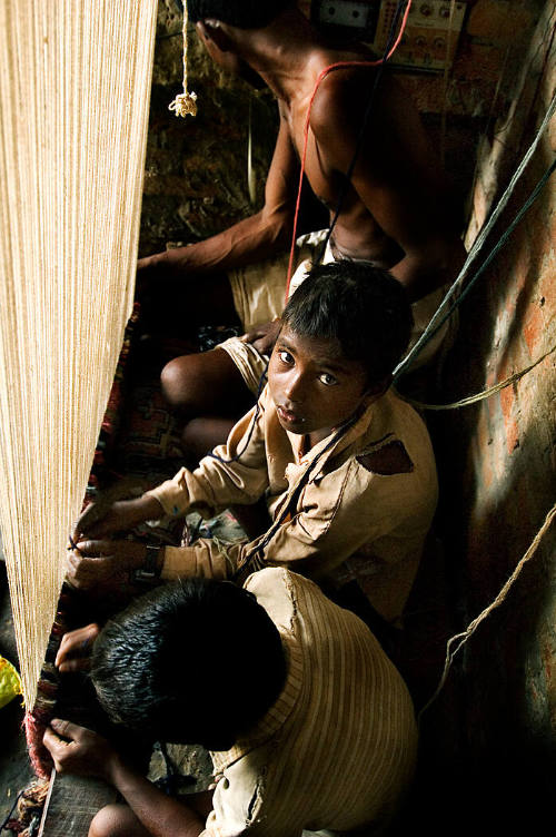 Borderless Captivity, Young boys work on carpet loom alongside father...